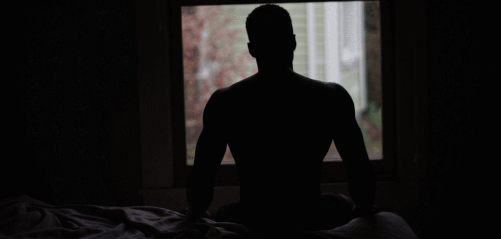 A Man Sitting in the Dark on the Edge of the Bed n the Nude Looking Out the Window