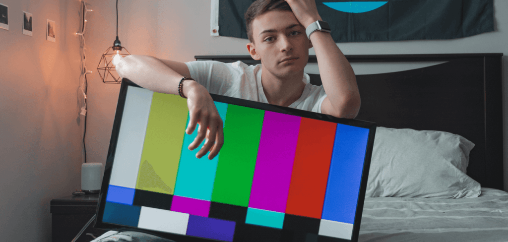 Young man sitting on the edge of the bed with a flat screen TV