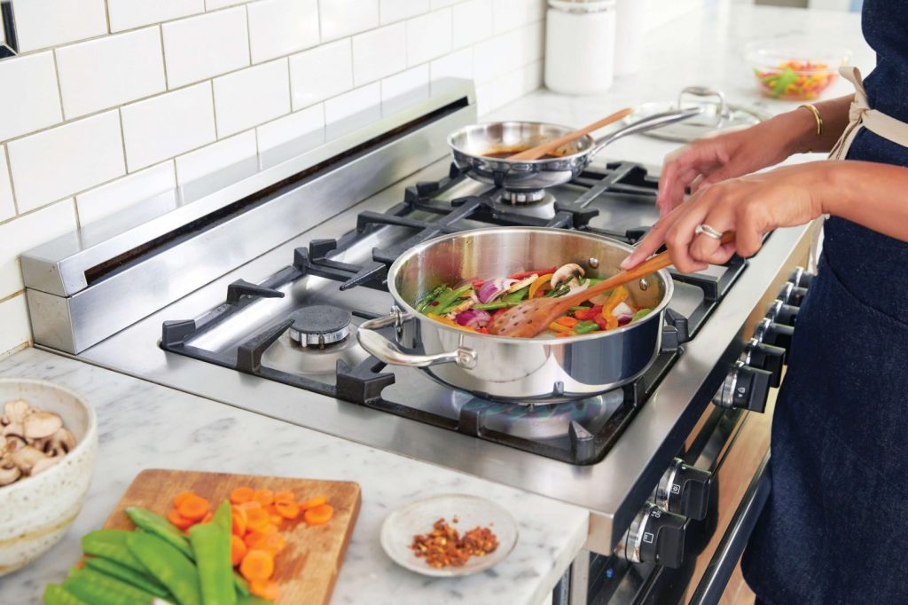 A woman in the kitchen cooking vegetables in a stainless steel pan on a stainless steal gas range