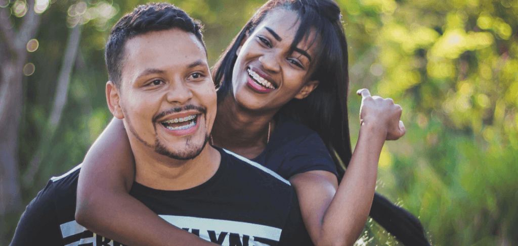 A woman on top a man's back with a black shirt both smiling with laughter