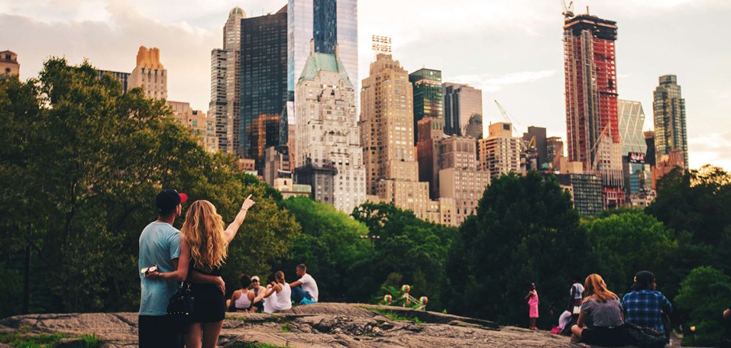 A couple in Central Park standing on a rock pointing at the city view from the park