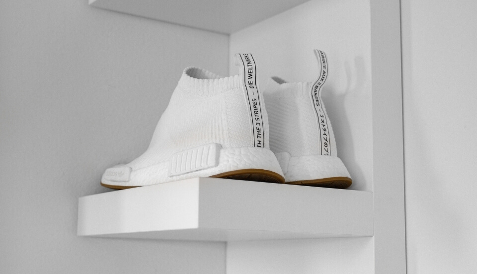 A pair of bright white sneakers on a white shelf against a white background