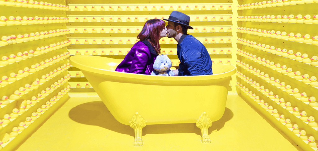 A beautiful couple kissing in a yellow tube in a yellow room surrounded by rubber ducks