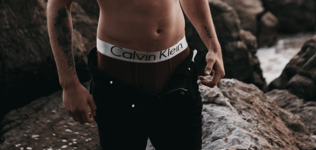 A shirtless man on the shore wearing Jeans with Calvin Klein Underwear Showing Slightly