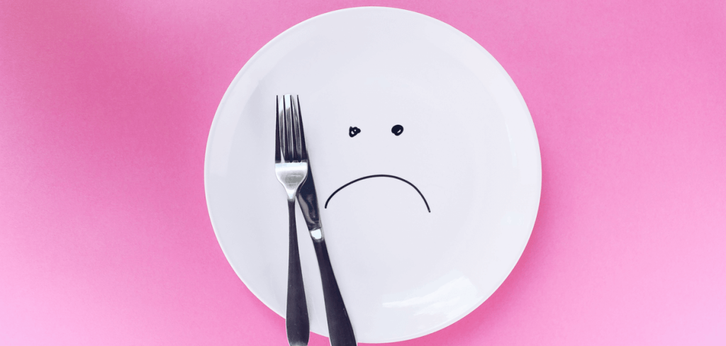 Silver fork and knife on a white place with a frown drawn on it
