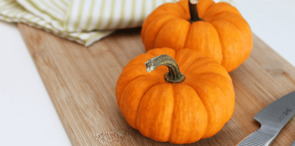 Two tiny pumpkins on a cutting board with a stainless steel knife