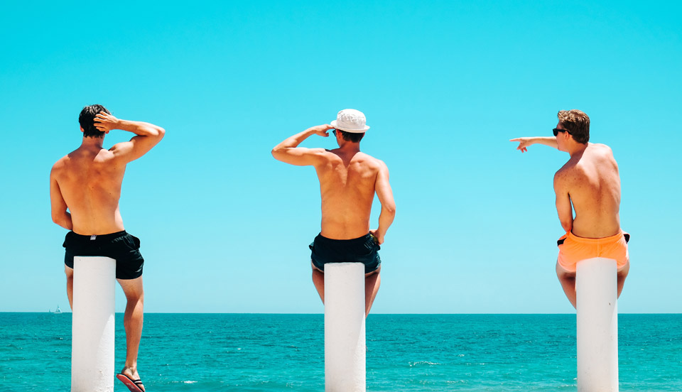 Three Friends Hanging out on the Beach in Torrevieja, Spain sitting on tall white poles and one guy is pointing toward the ocean.