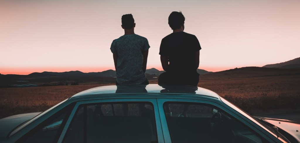 Two guys seating on the roof of a car looking at the sunset