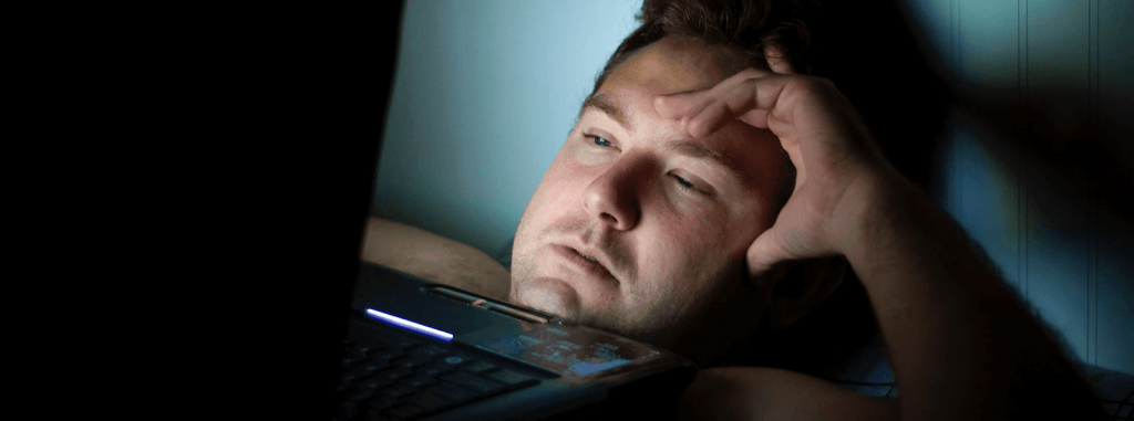 Man laying the bed in the dark looking at his laptop screen