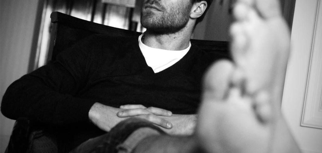 A bearded man bare-footed with his legs crossed