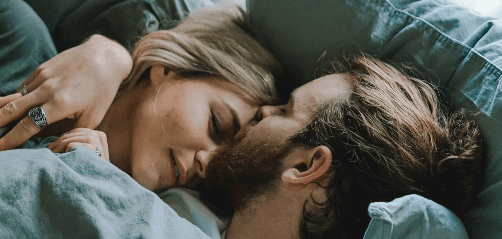 Man Kissing A Woman's Forehead While Laying in Bed