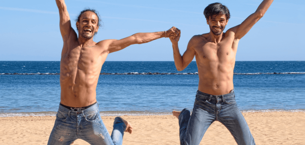 Two men in love jumping above brown sand during the summer