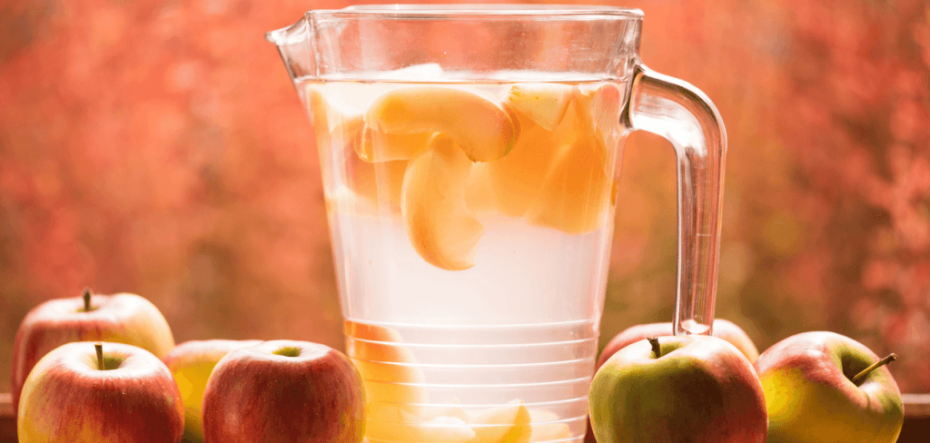 A glass pitcher surround apples