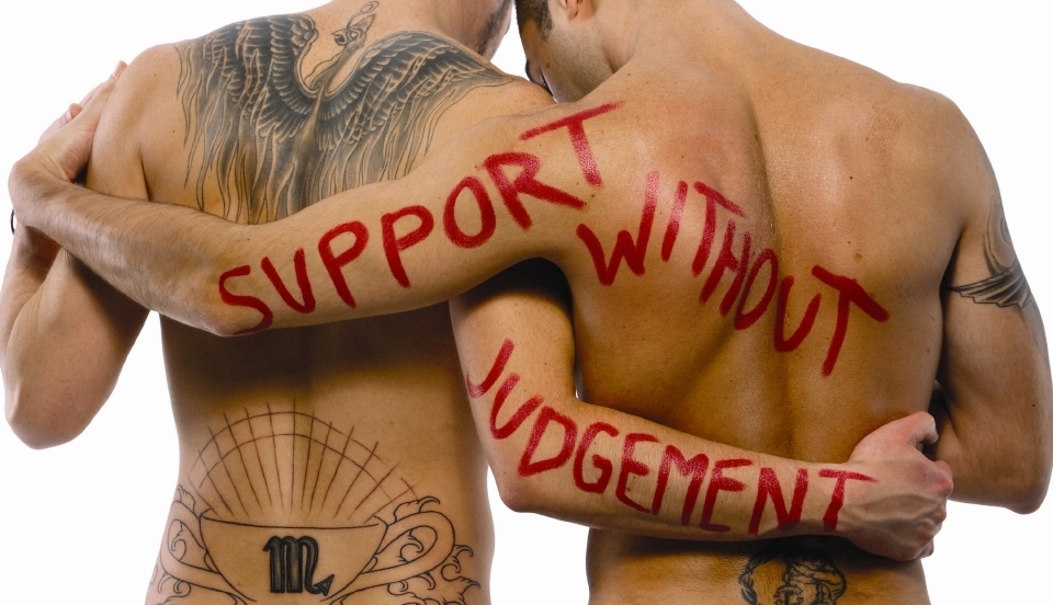Two men holding each other with showing their back with support without judgement written in red lipstick