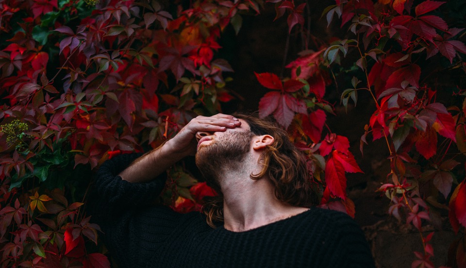 A man covering his eyes standing in front of a wall of roses thinking about life and love
