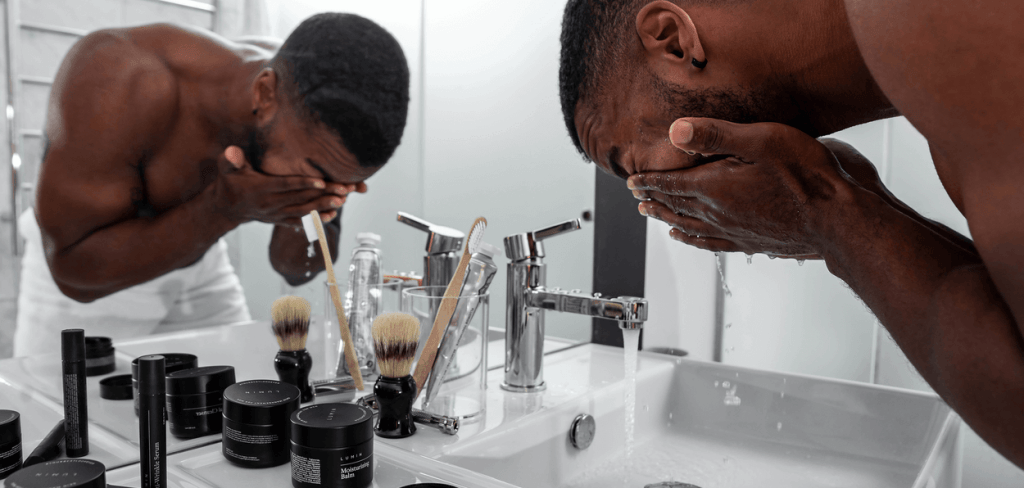 A Handsome African-American in an All White Bathroom Washing His Face with Skincare Products
