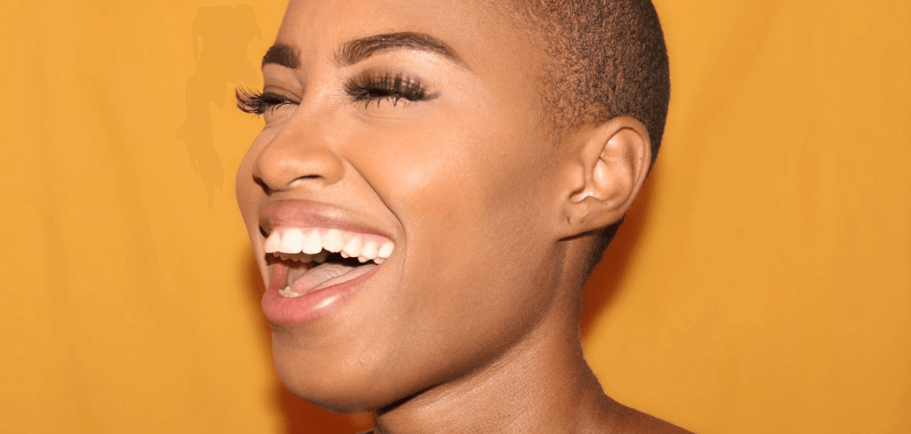 Beautiful African-American Woman With A Buzz Cut Smiling Against a Yellow Background