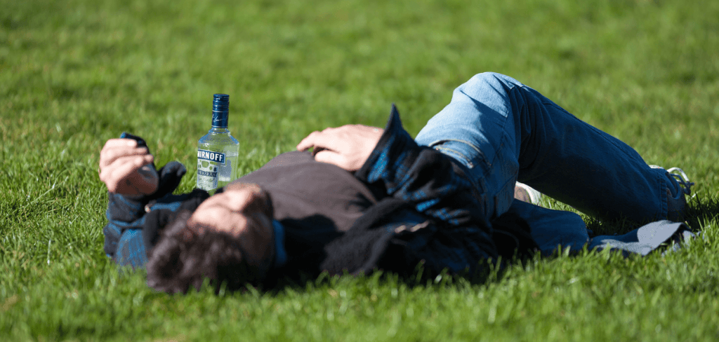 Party Patch: A white man with a hangover on the grass with a vodka bottle next to him - OVAH MAG