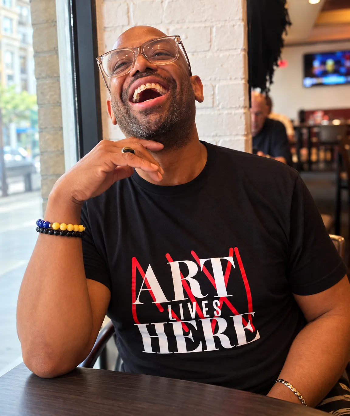 Corey Wesley laughing in clear glasses and a black Art Lives Here shirt