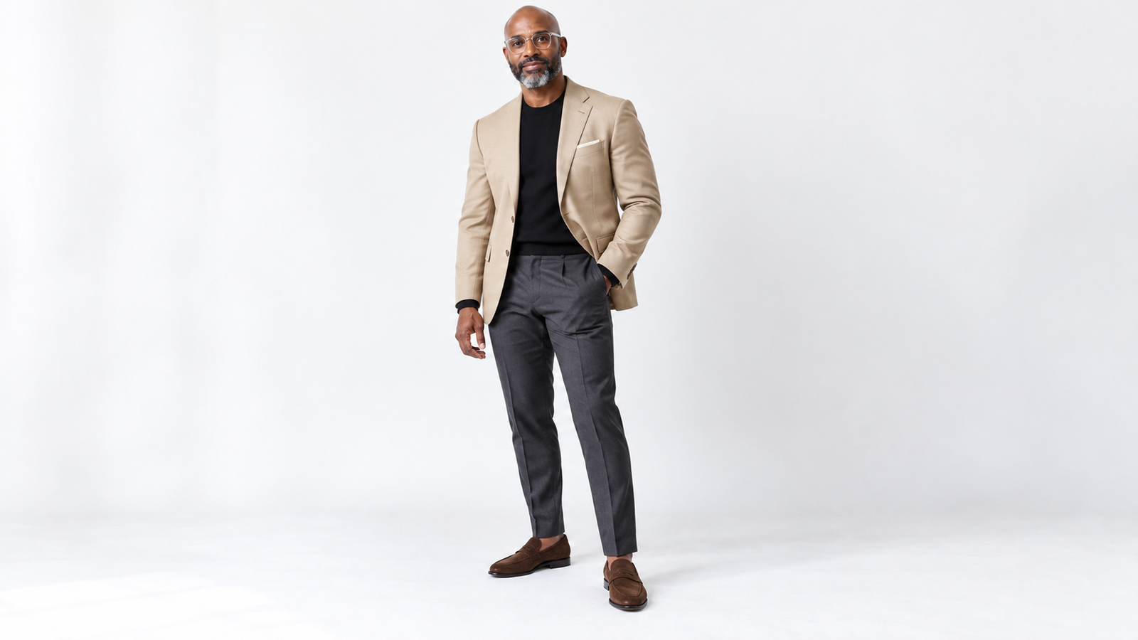 Man in a khaki blazer, black crew-neck sweater, charcoal gray trousers and brown suede loafers, one look from a navy, charcoal and khaki suit palette
