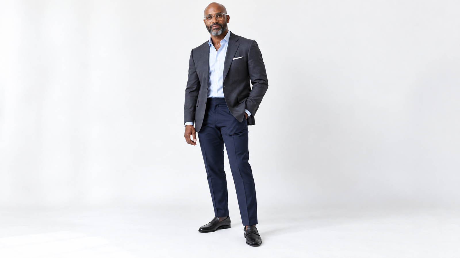 Man in a charcoal gray blazer, light blue shirt, navy trousers and black loafers, one look from a navy, charcoal and khaki suit palette
